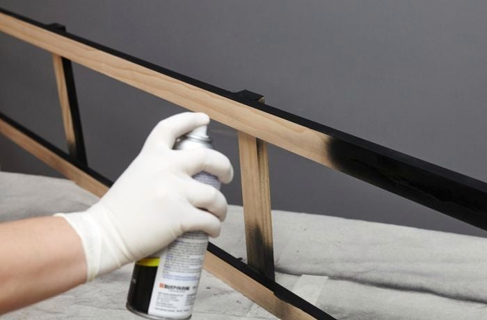 Person spray painting timber book shelf side black.