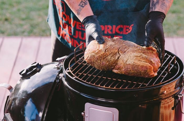 Person in apron place pork shoulder on the rack of a smoker