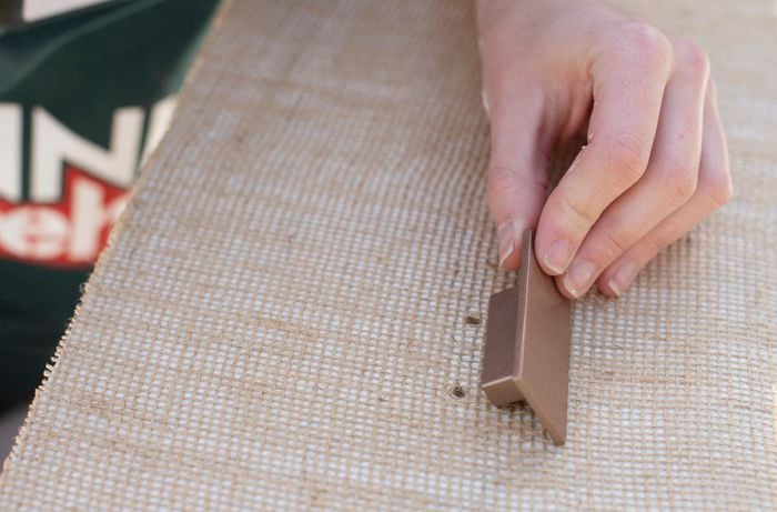 Person attaching a handle to a drawer covered in hessian