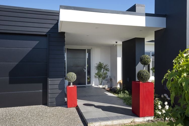 Exterior of a house painted black and white with two red planters and a dark grey front door