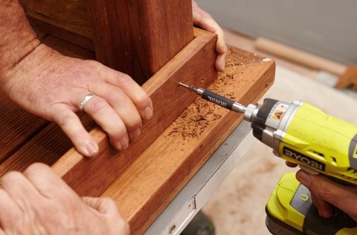 Two people working together to drill a wooden table leg and top together.