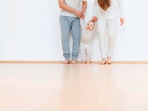 A mother, father and child stand together on a floor.