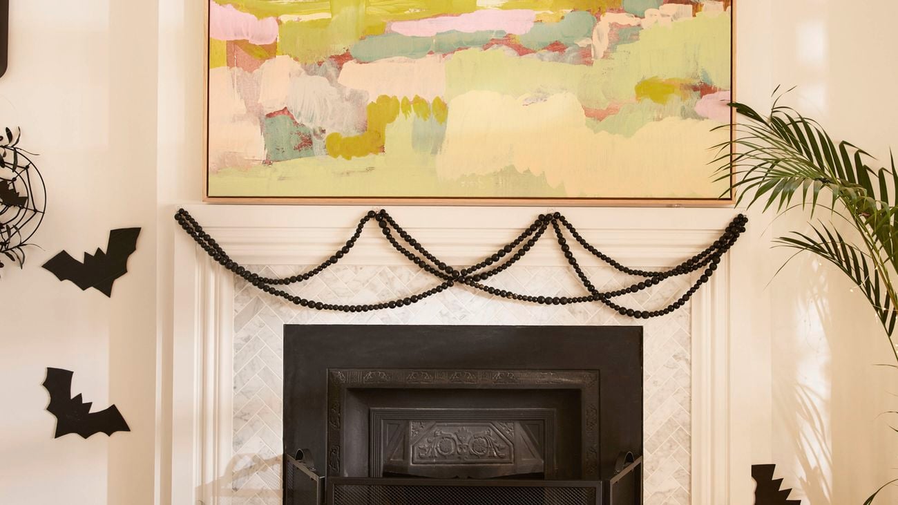 A fireplace decorated for Halloween with black bat cut-outs and bead garlands. A large colourful painting hangs above the mantel