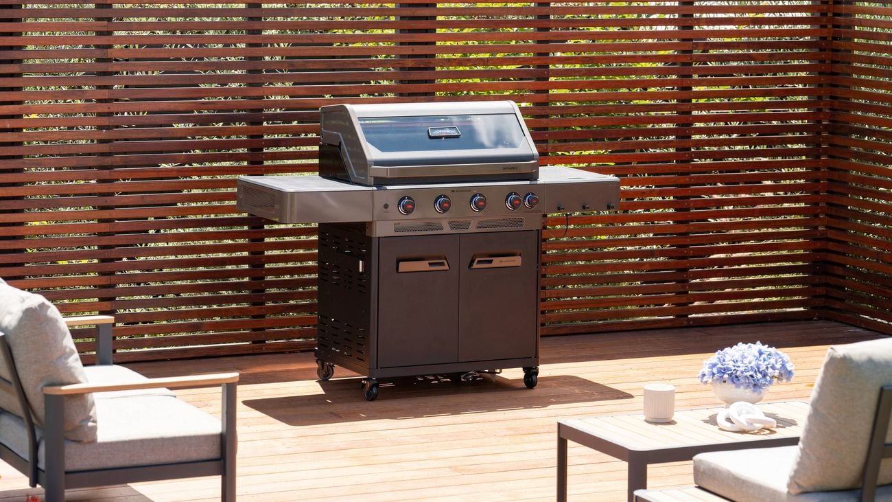 A barbecue on a timber decking with an outdoor setting in front of it.