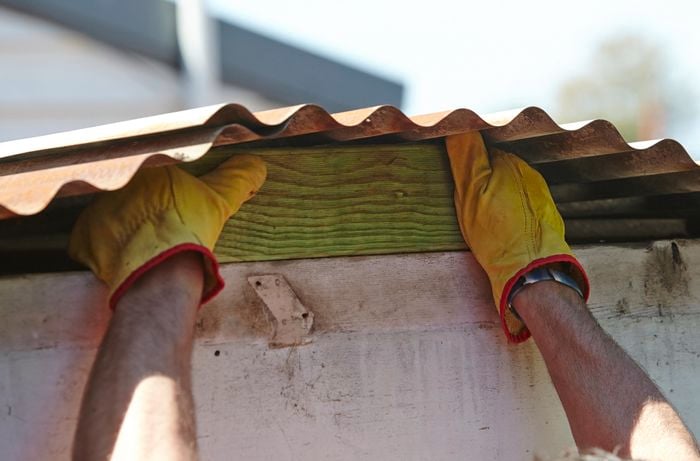 A person placing a timber block underneath corrugated roofing to prop it