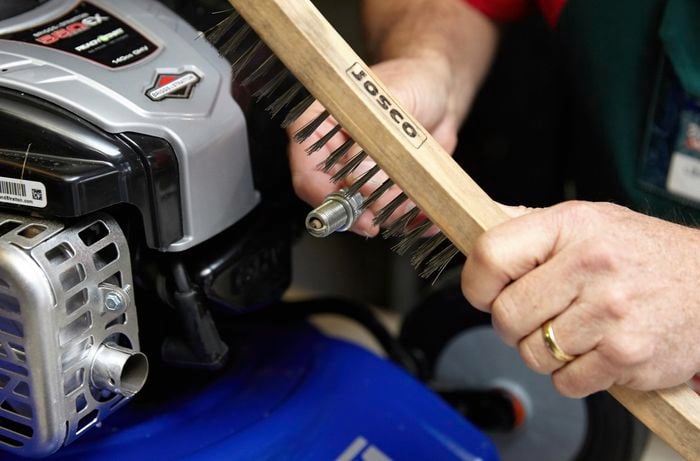 A person cleaning a spark plug with a wire brush