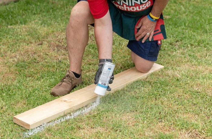 Bunnings team member spray painting a line with a piece of timber as a guide