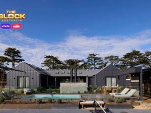 The back of a house with a pool in it, outdoor lounge, rocks area and an outdoor fireplace in i