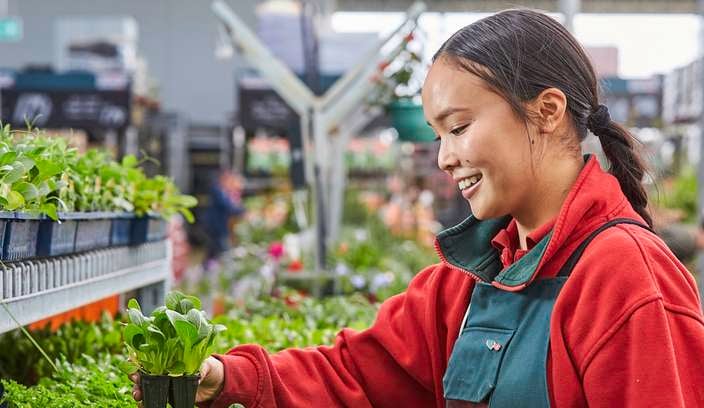 Team member in nursery picking up a seedling and smiling