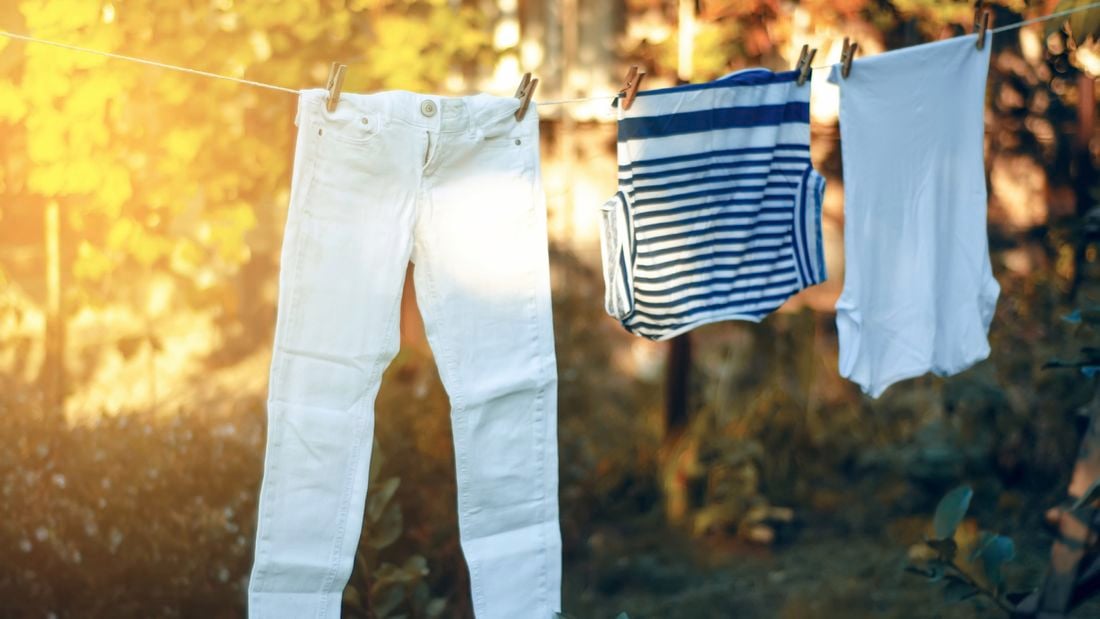 A pair of white jeans, a striped top and plain white t-shirt hang on a clothesline.