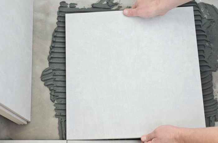 Close up of a person placing a tile against wet concrete