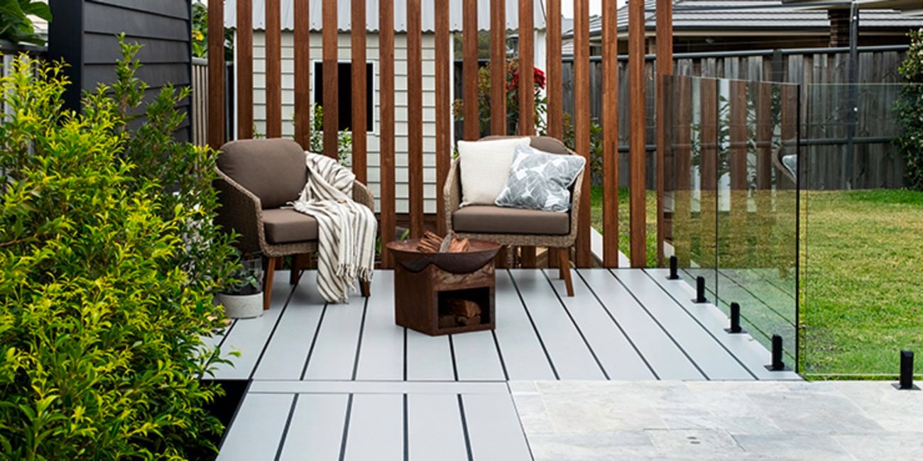 Pool surrounded by timber decking with two chairs and a firepit