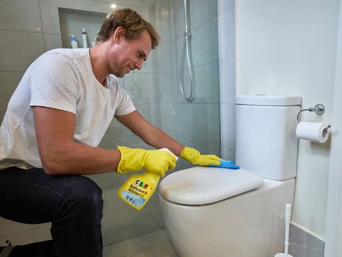 A man holding a bottle of CLR Bathroom & Kitchen Foaming Action Cleaner above a toilet.