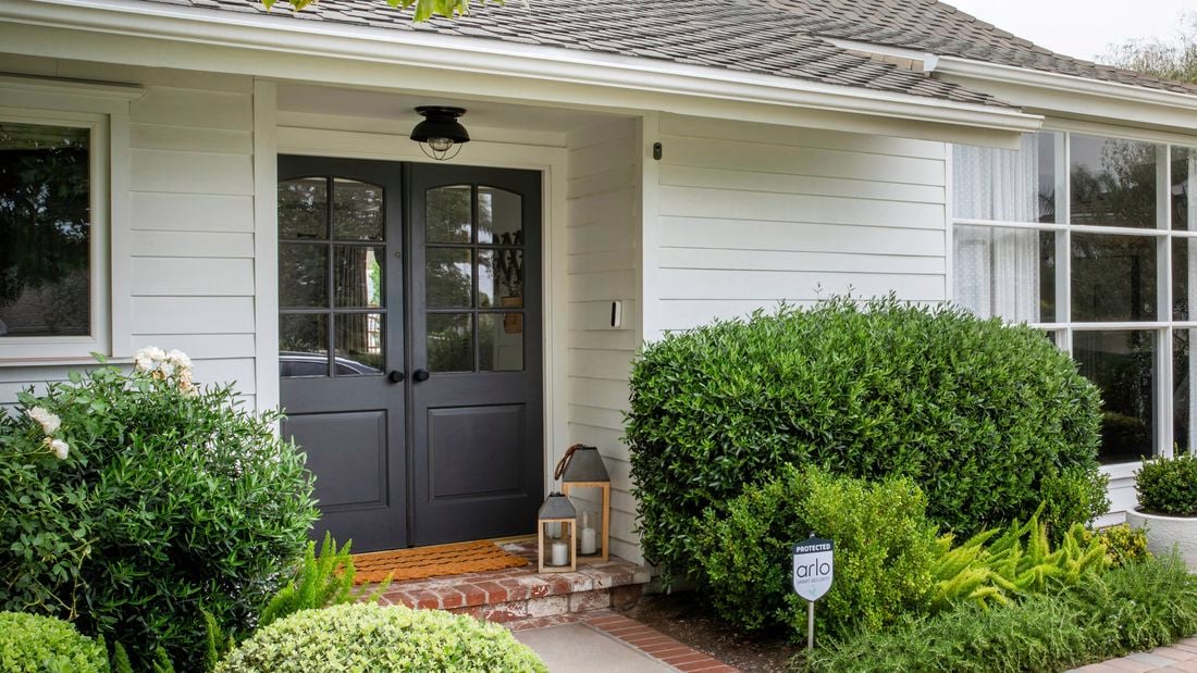 Front entrance of a suburban house with a doorbell camera, home security camera, front porch and shrubs.