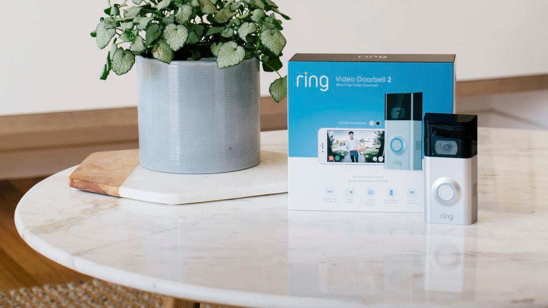 Ring Video Doorbell 2 sitting on a marble table next to it's box and a small potted plant