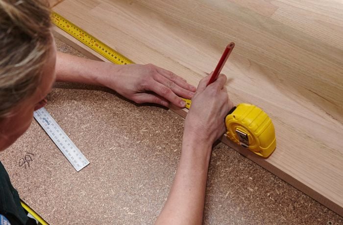A person marking a measurement onto a timber panel using a measuring tape