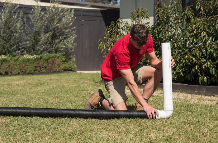 A Bunnings Team Member is installing a vertical PVC pipe with an elbow joint.