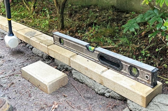 Pavers laying on fresh mortar with a spirit level on top and two work-booted feet in shot