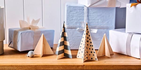 Four completed balsa wood Christmas tree figurines on a wooden table surrounded by Christmas presents