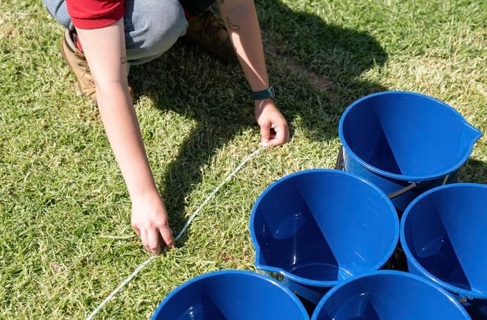 Person lining up blue buckets along a line.