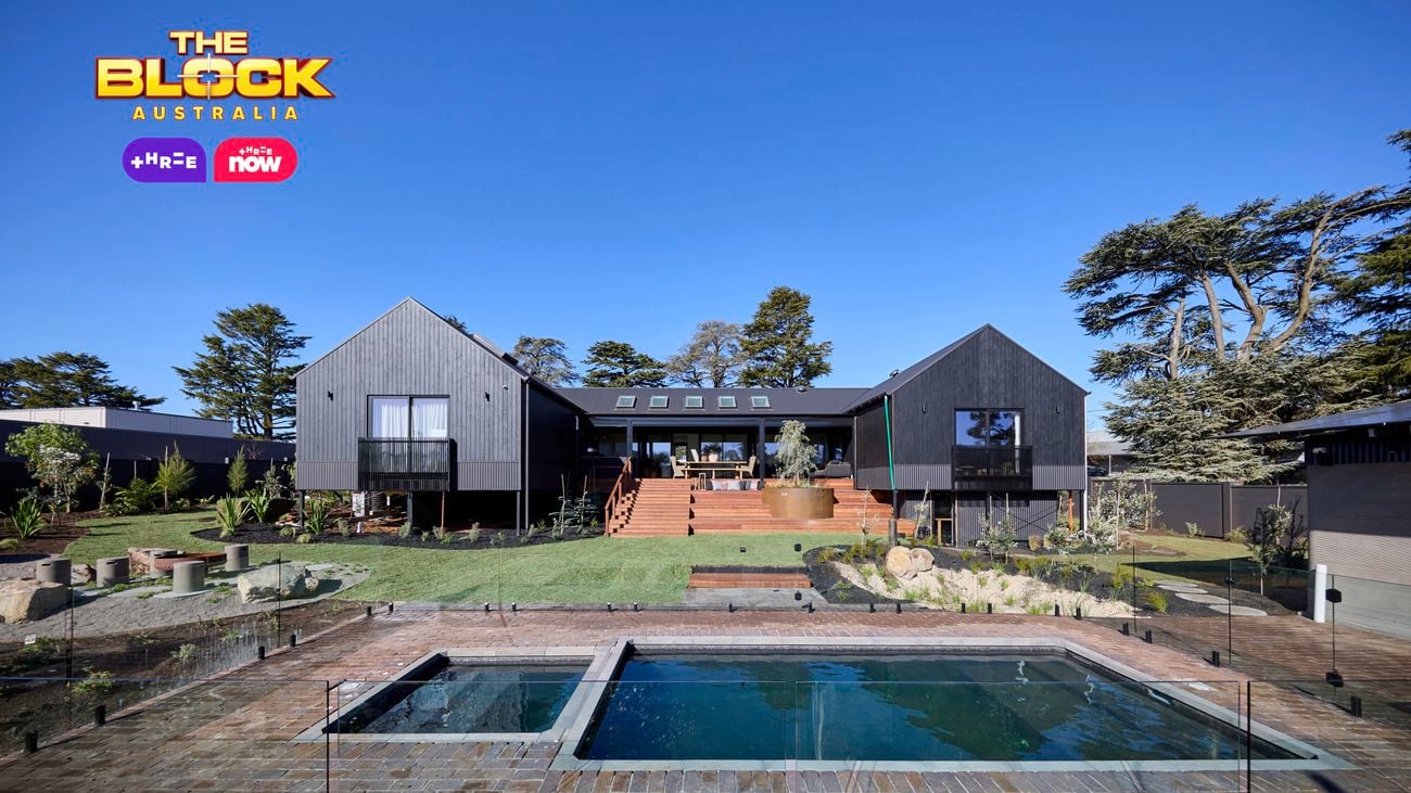 The back of a house with a pool in it, a rocked area, timber decking and many plants in it.