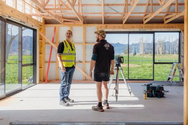 Two builders chatting on a building site, one wearing a cap and in high fluo vests hard hats