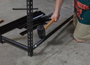 A person using a rubber mallet to assemble steel shelving