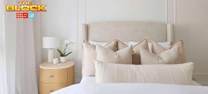 A furnished bedroom with a bed and bedside table with a lamp and pot plant on it in it and The Block logo in the image.