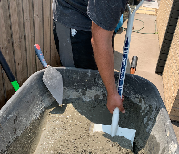 Person mixing mortar in a wheelbarrow with long handle shovel