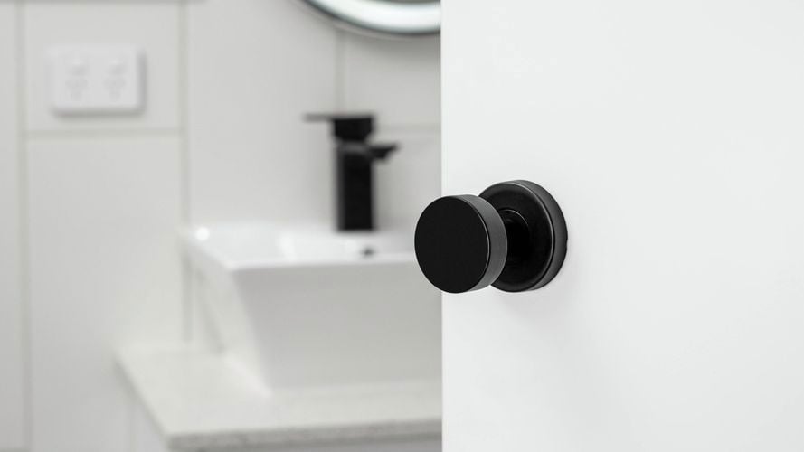 A Delf Marbella Knob Set Matte Black doorknob open to a bathroom