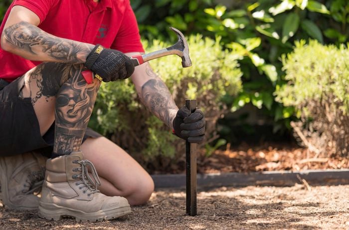A Bunnings Team Member is placing a setback stakes one metre away from each corner mark using a hammer. 