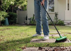 A person wearing jeans sweeping an outdoor garden path with an Oates broom