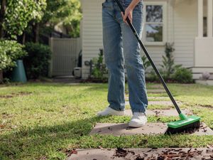 A person wearing jeans sweeping an outdoor garden path with an Oates broom