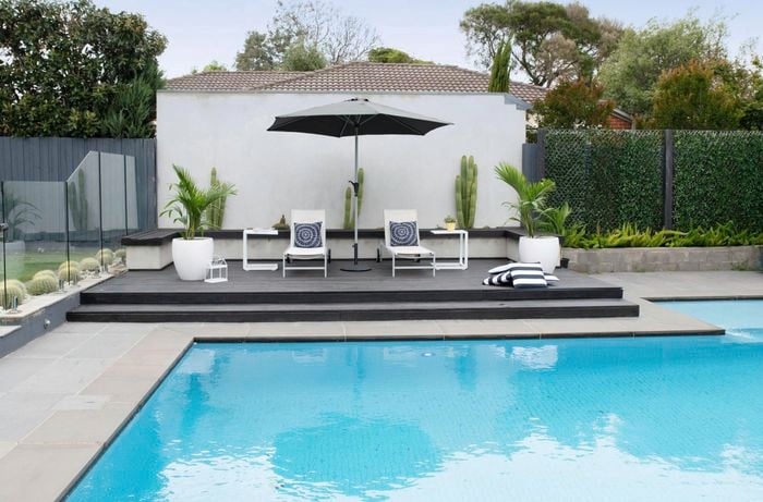 A wide shot of an outdoor pool area, with umbrella, sunbeds and throw cushions