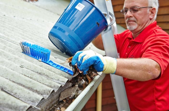 Person on a ladder clearing leaves out of a roof gutter