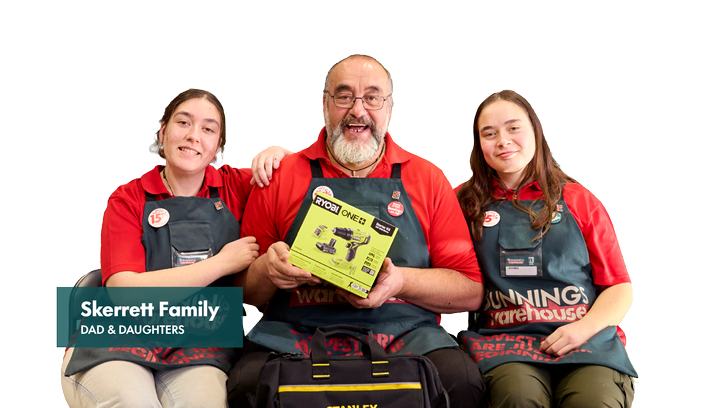 Three Bunnings team members seated together against a light grey background, wearing red polo shirts and dark green Bunnings Warehouse aprons. The person in the centre holds a Ryobi ONE+ power tool kit box. A teal text panel reads “Skerrett Family, Dad & Daughters.”