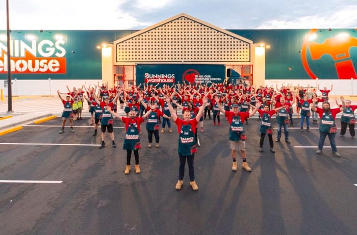 Bunnings team members with aprons with their hands in the air, at the front of a Bunnings store