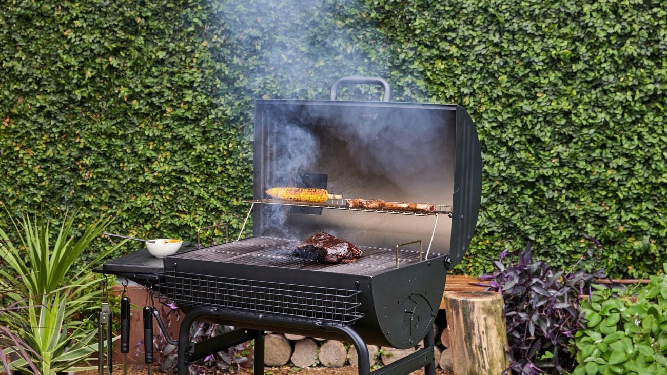 Charcoal grill with it’s top open being used to cook various foods, with smoke surrounding it