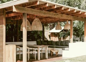  Outdoor living area with a wooden pergola, L-shaped sofa, dining table and lush tropical greenery.