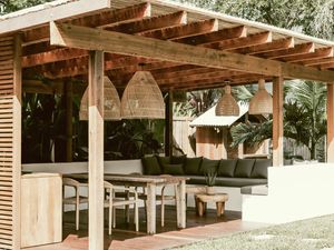  Outdoor living area with a wooden pergola, L-shaped sofa, dining table and lush tropical greenery.
