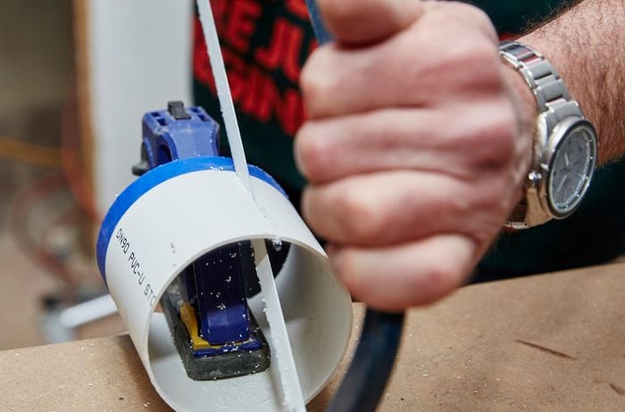 A person sawing lengthwise through PVC pipe using a hacksaw