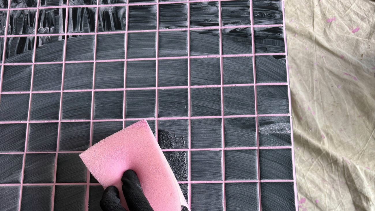 A gloved hand using a pink sponge to clean the tiles.