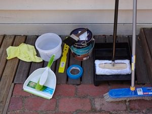 Paint brushes, mop, tape and other painting items on a wooden desk outside.