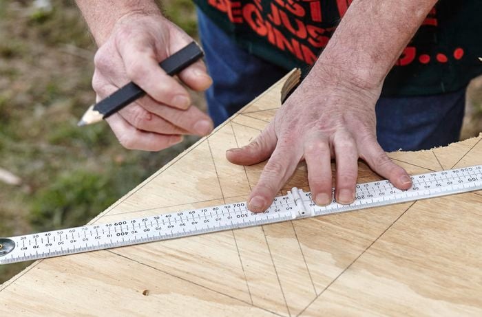 A person marking diagonal lines on a sheet of plywood