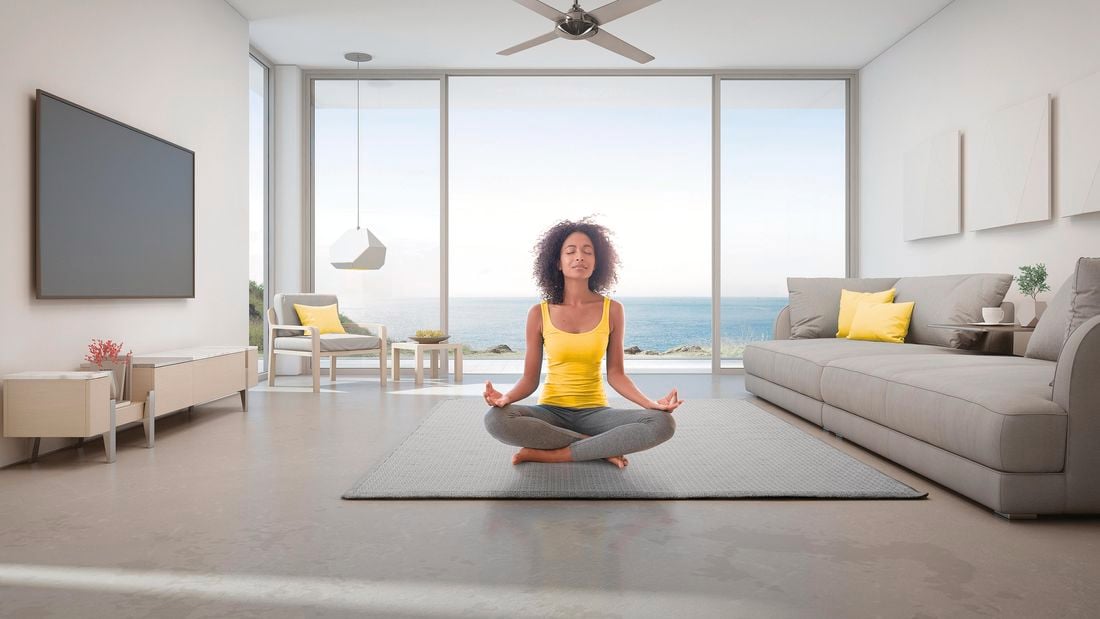 A woman meditating underneath a ceiling fan in a room overlooking the ocean