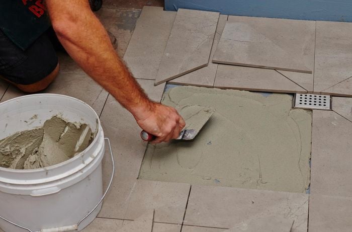 A person using a trowel to spread adhesive on a shower base