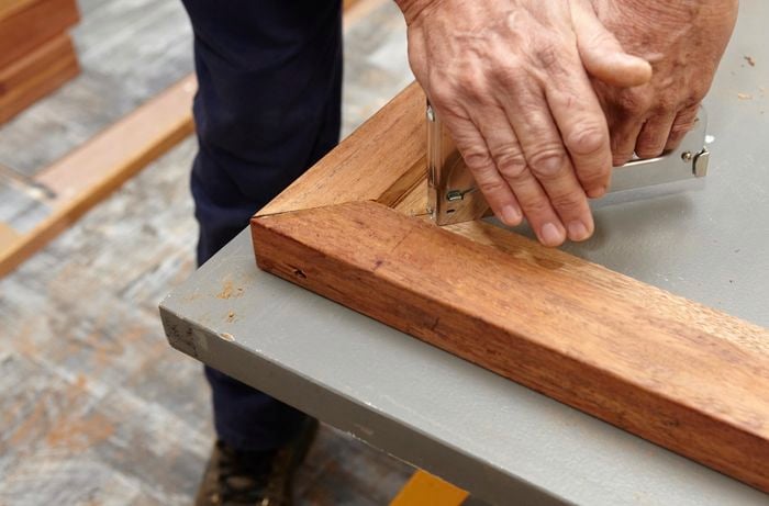 Person stapling corners of timber frame together.