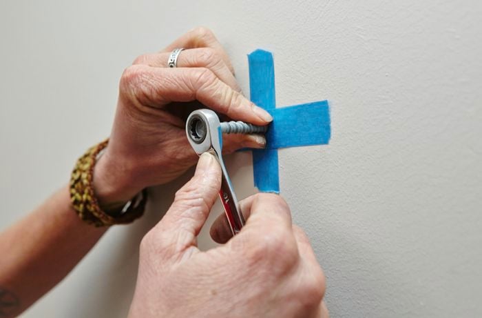 A person installing a masonry bolt in a wall using a spanner