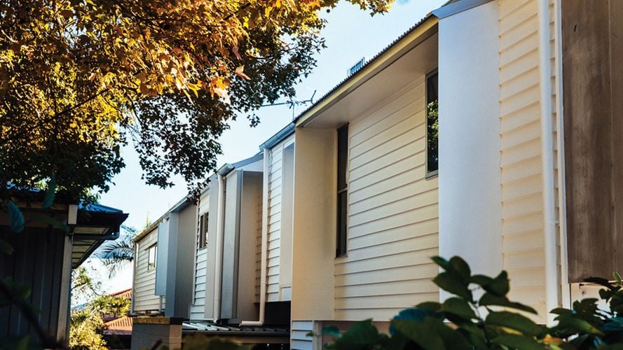 Exterior of a weatherboard house painted off-white with a tree to one side