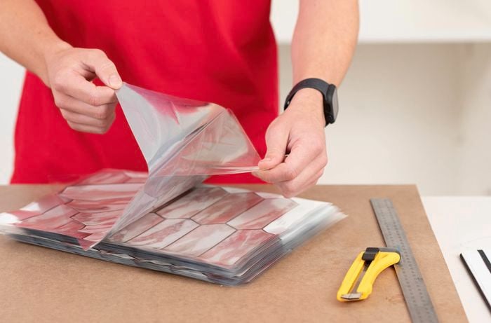 A person in a red T-shirt is removing adhesive tiles